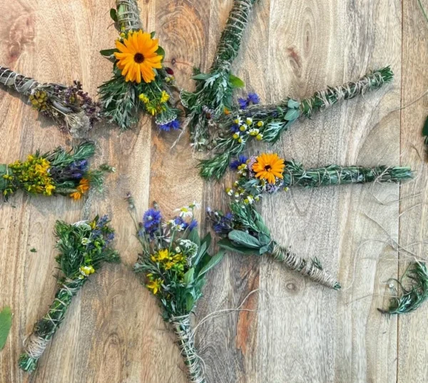 Handgebundene Räucherbündel aus frischen Wildkräutern und Blüten liegen auf einem Holztisch.